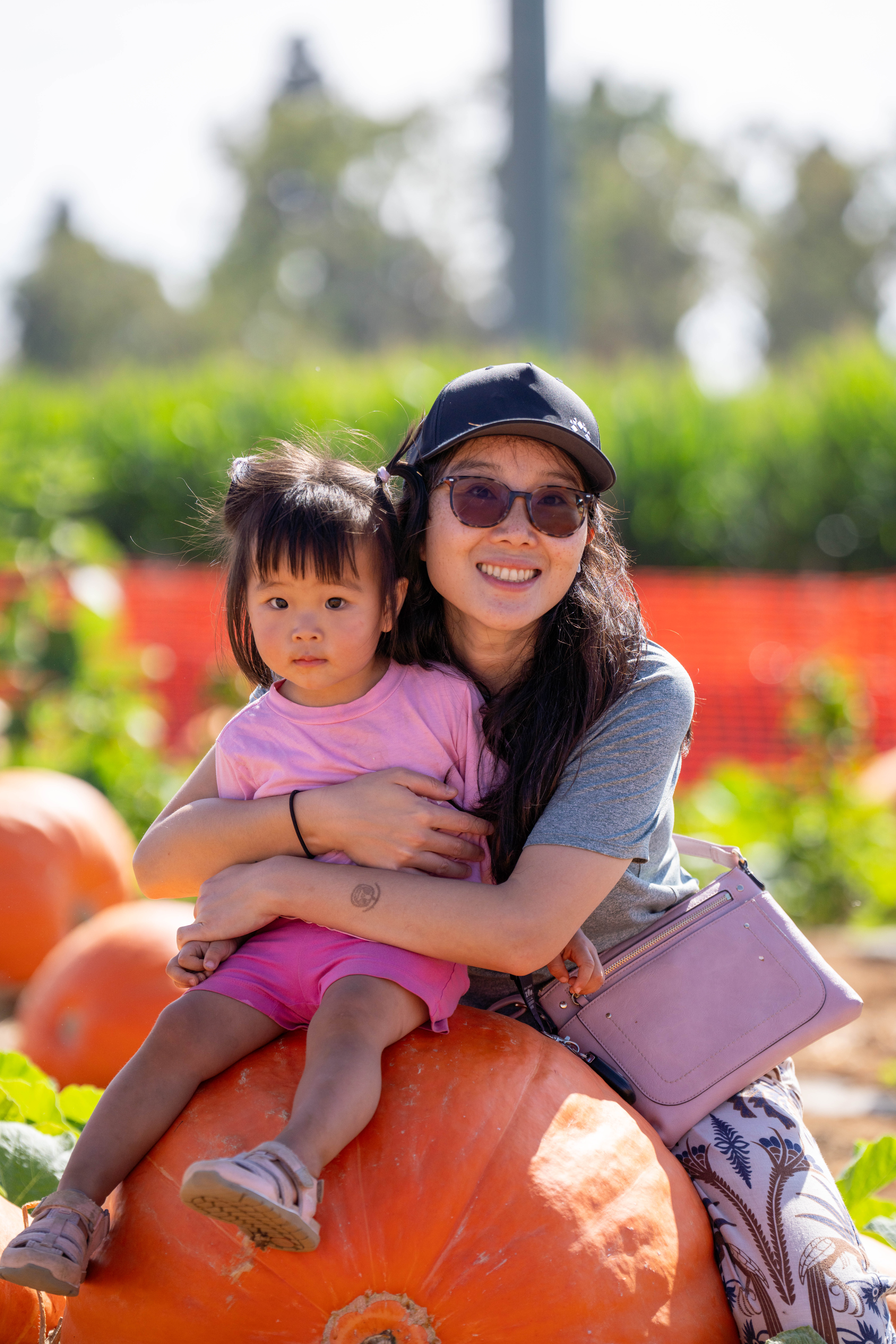Mom and toddler daughter smiling together on top of a large pumpkin