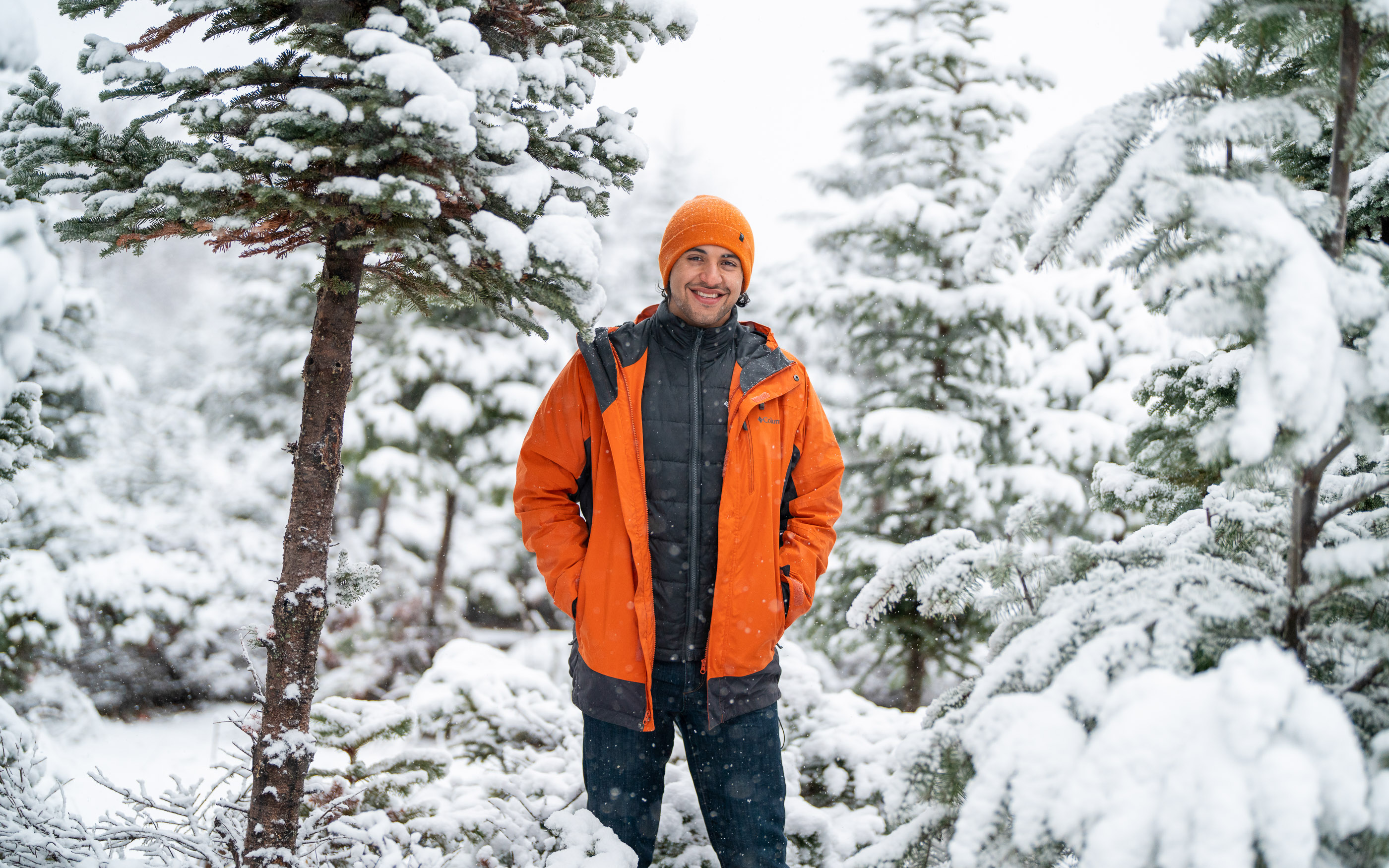 Photographer standing in a snowy forest wearing an orange jacket and beanie