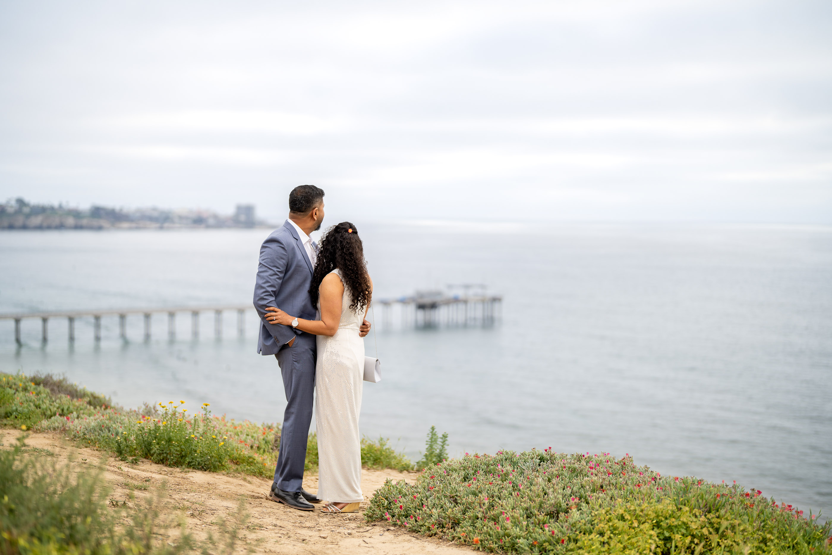 Couple standing together on a grassy coastal bluff overlooking the ocean