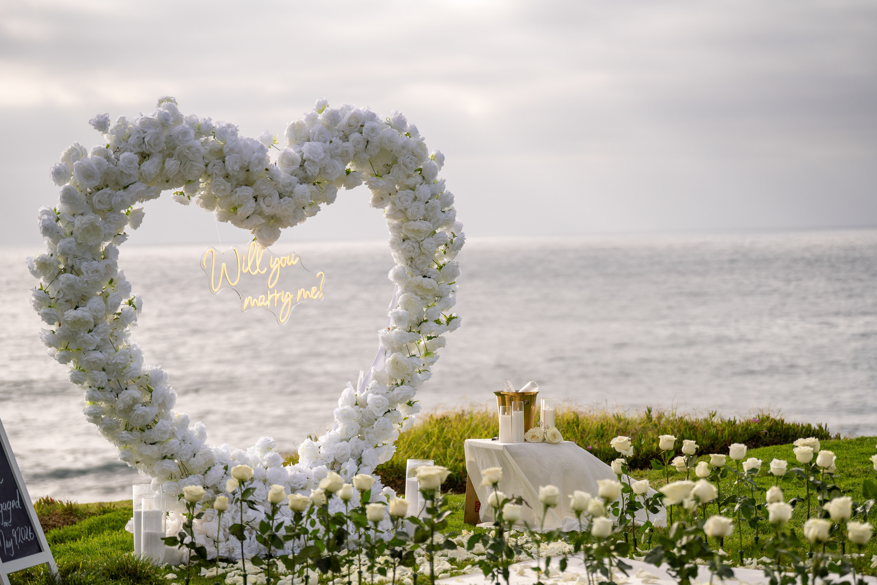White floral heart-shaped arch overlooking the ocean during a romantic proposal setup