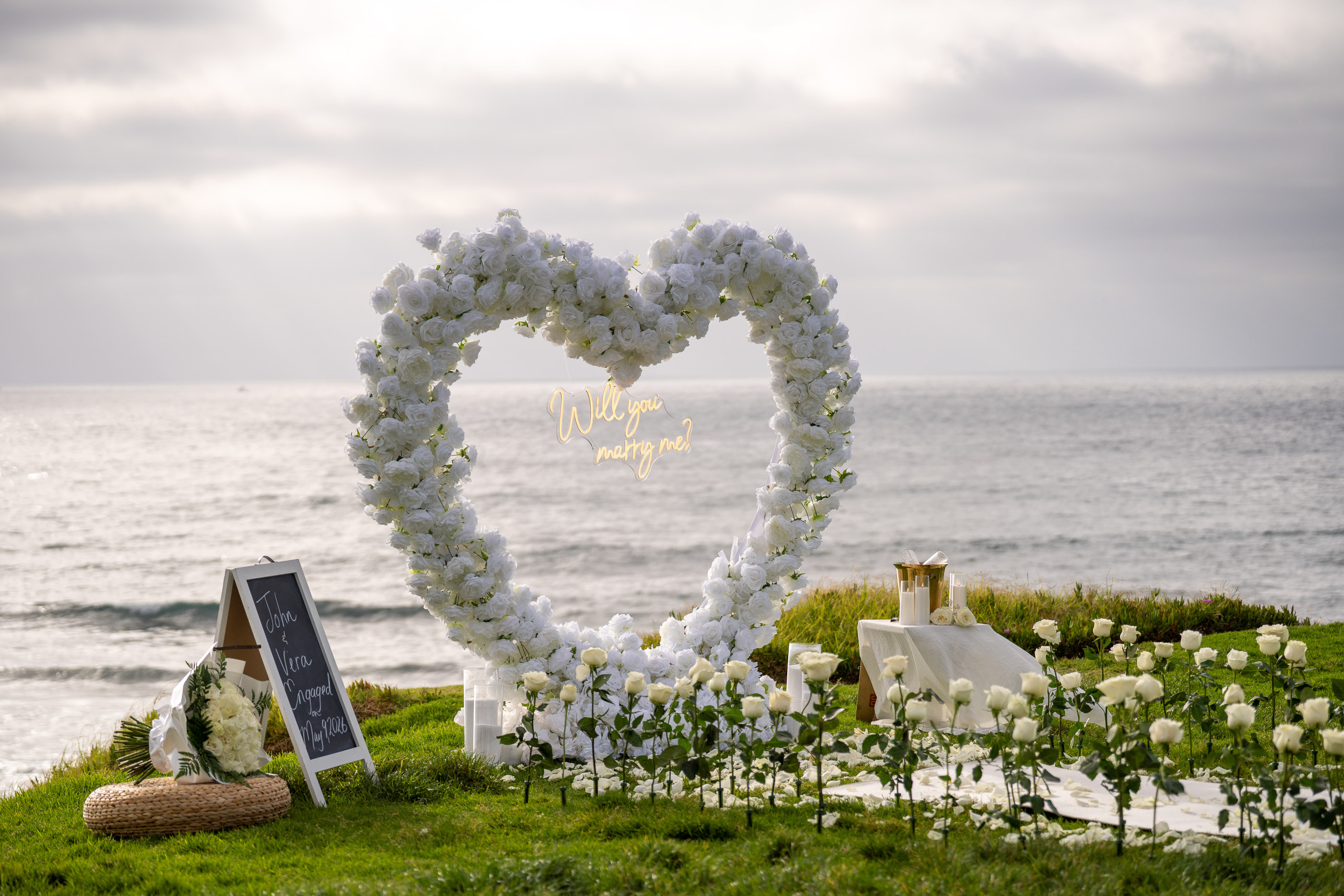 Romantic proposal setup with a white floral heart overlooking the ocean