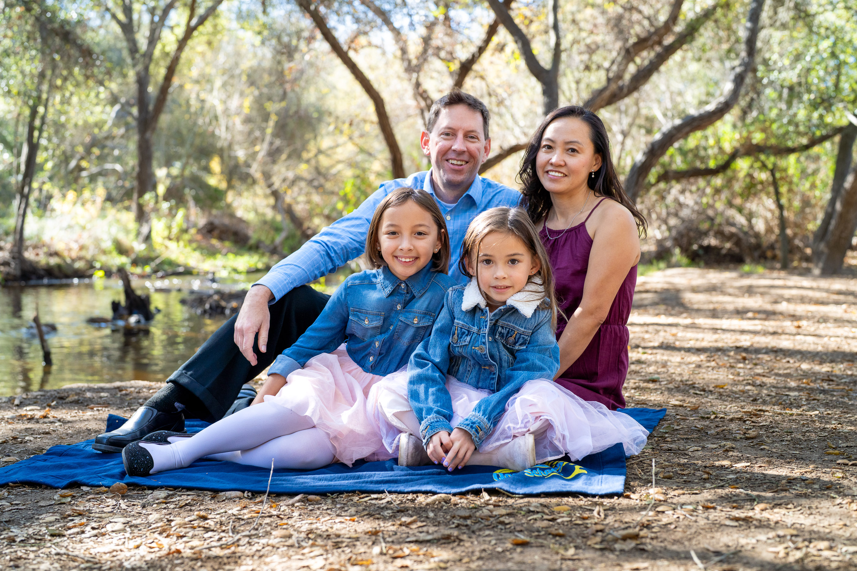 Family sitting together on a blanket beneath trees in a peaceful outdoor setting