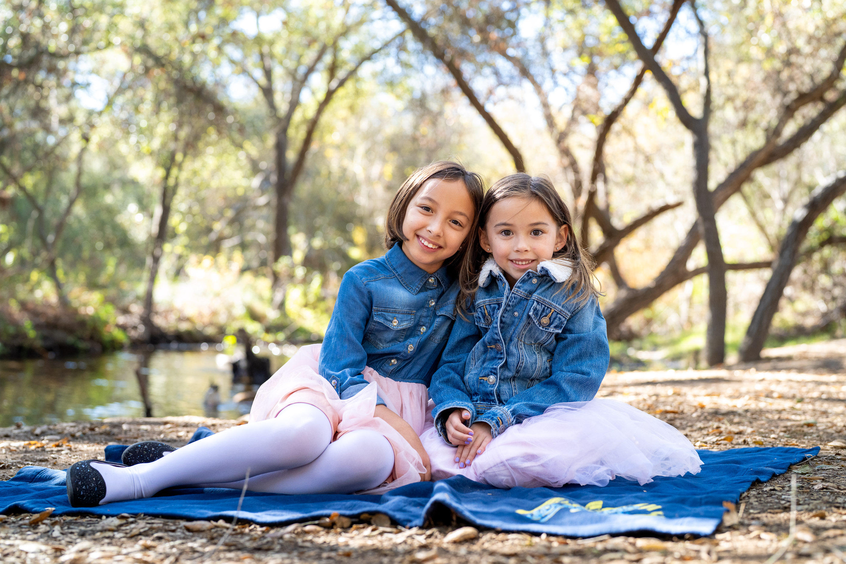 Two young sisters sitting together and smiling on a blanket outdoors