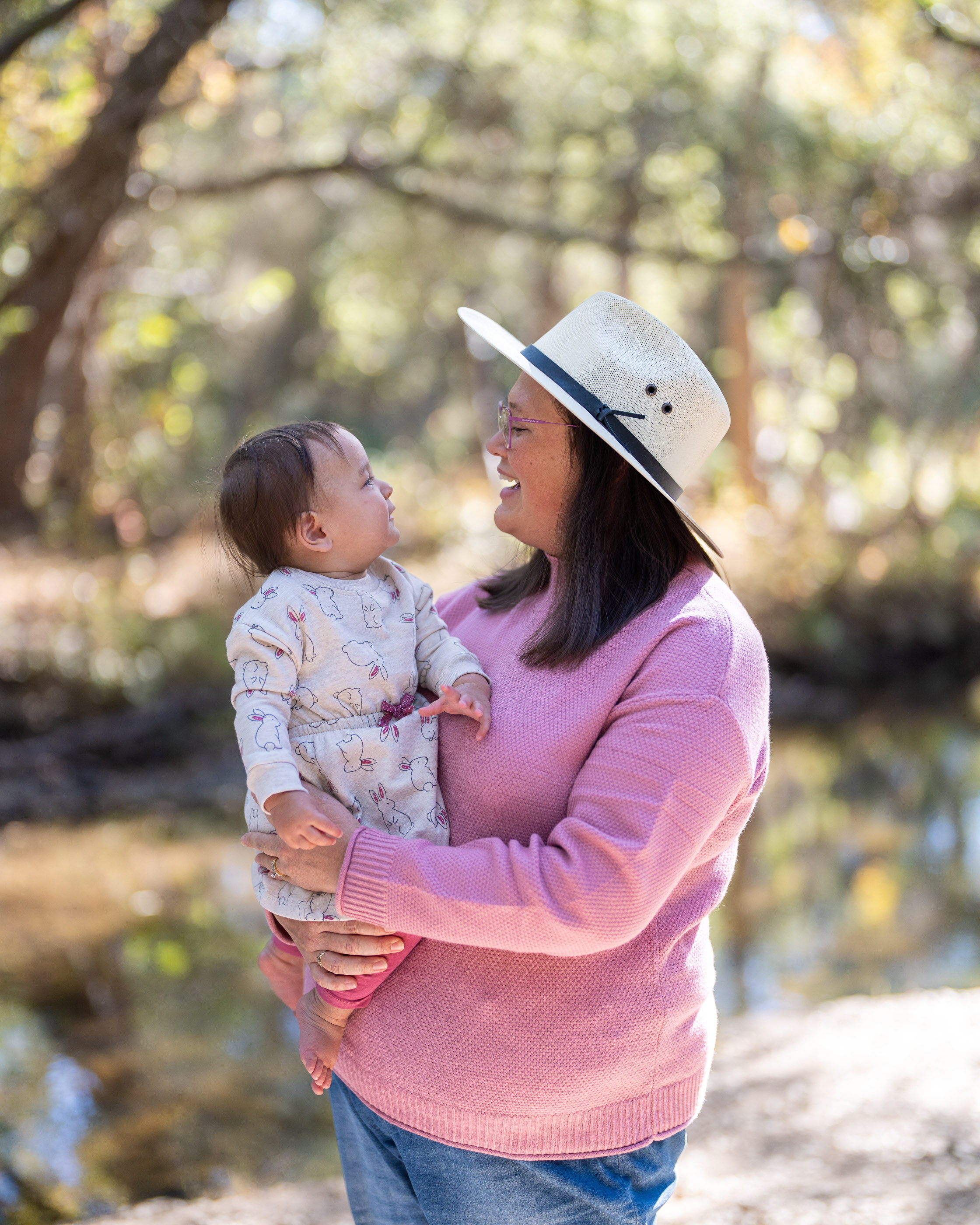 Mother holding her young daughter outdoors beneath tall trees