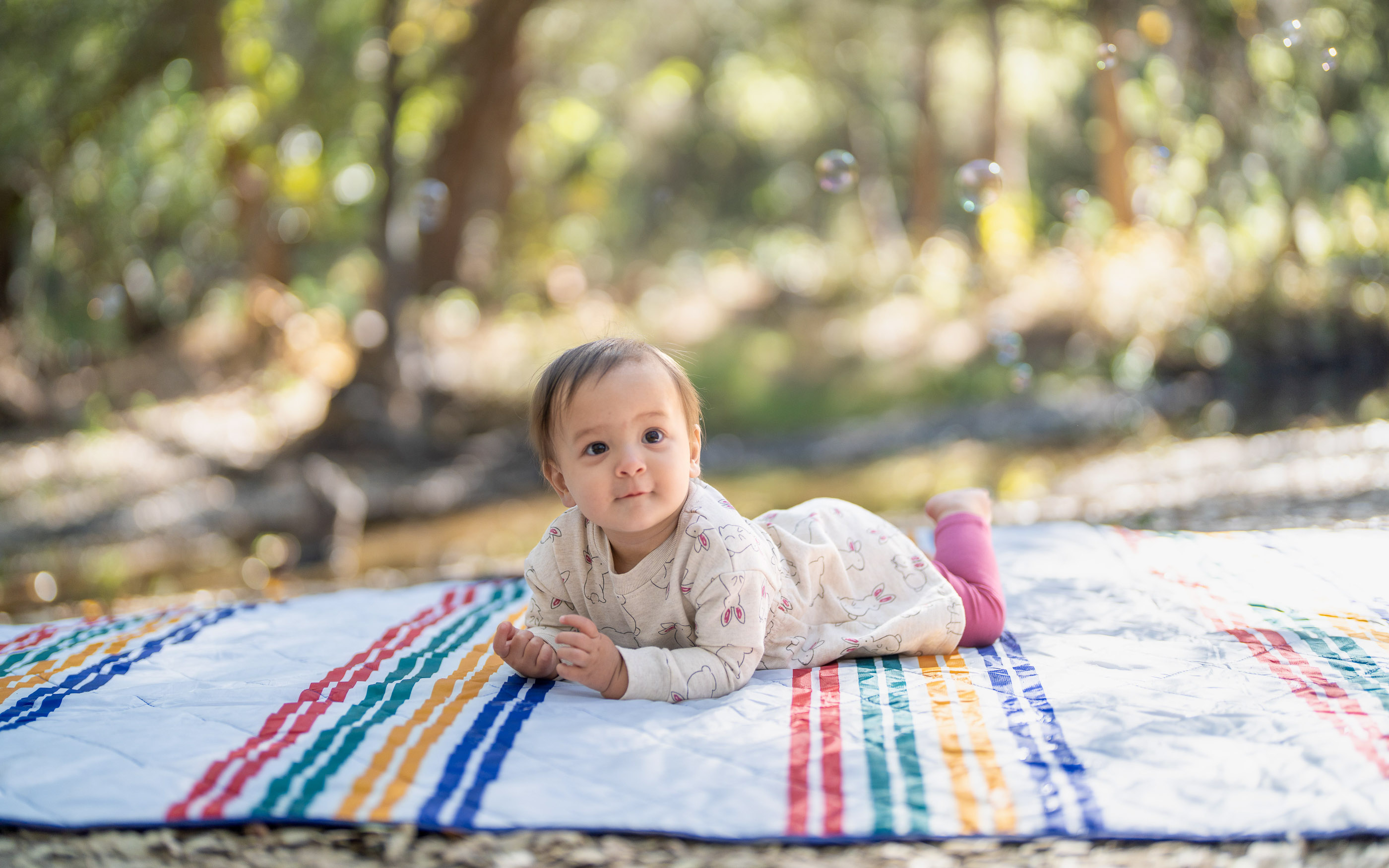 Baby lying on a colorful blanket outdoors in a wooded setting