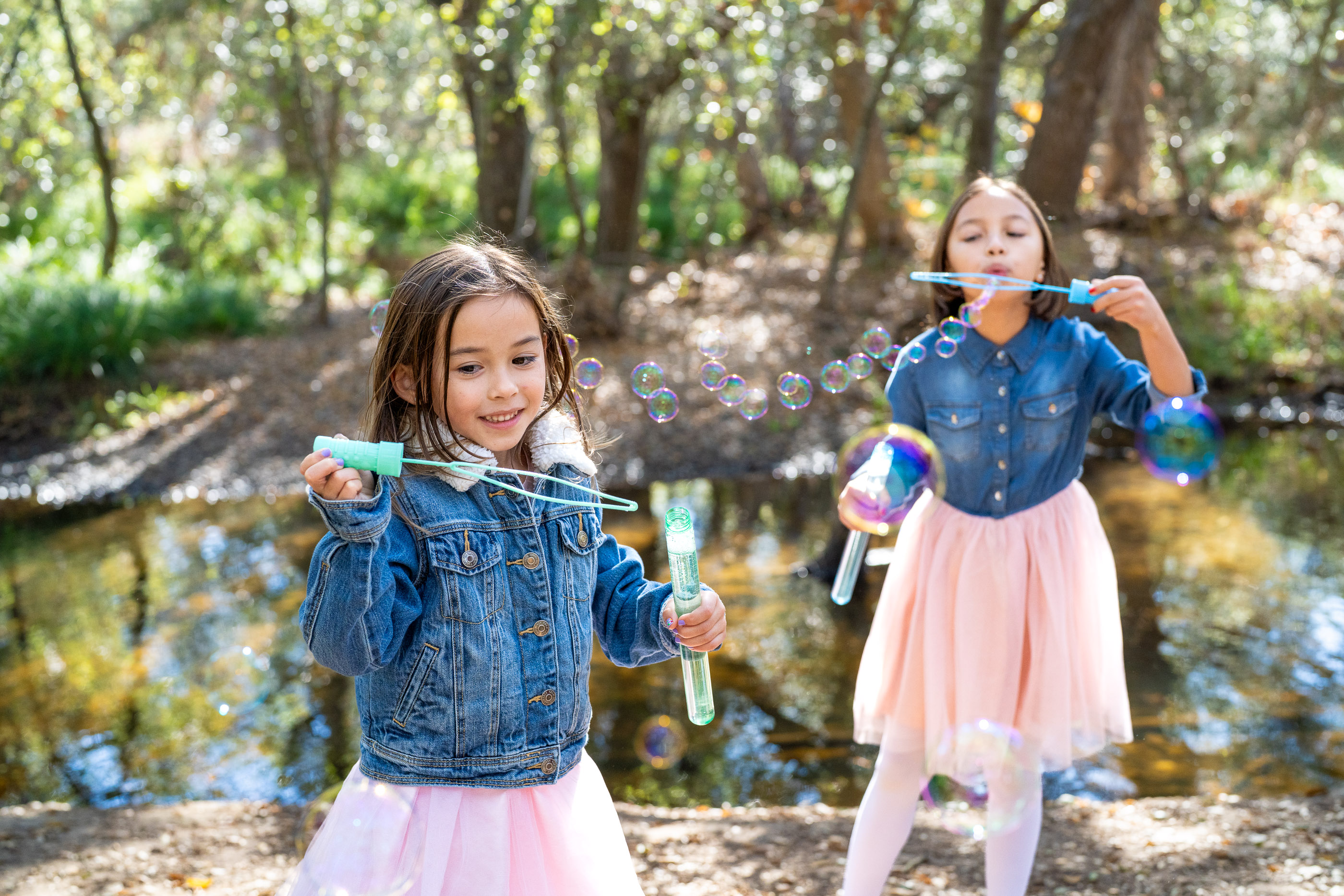 Two young girls playing together beside a shallow creek in the woods
