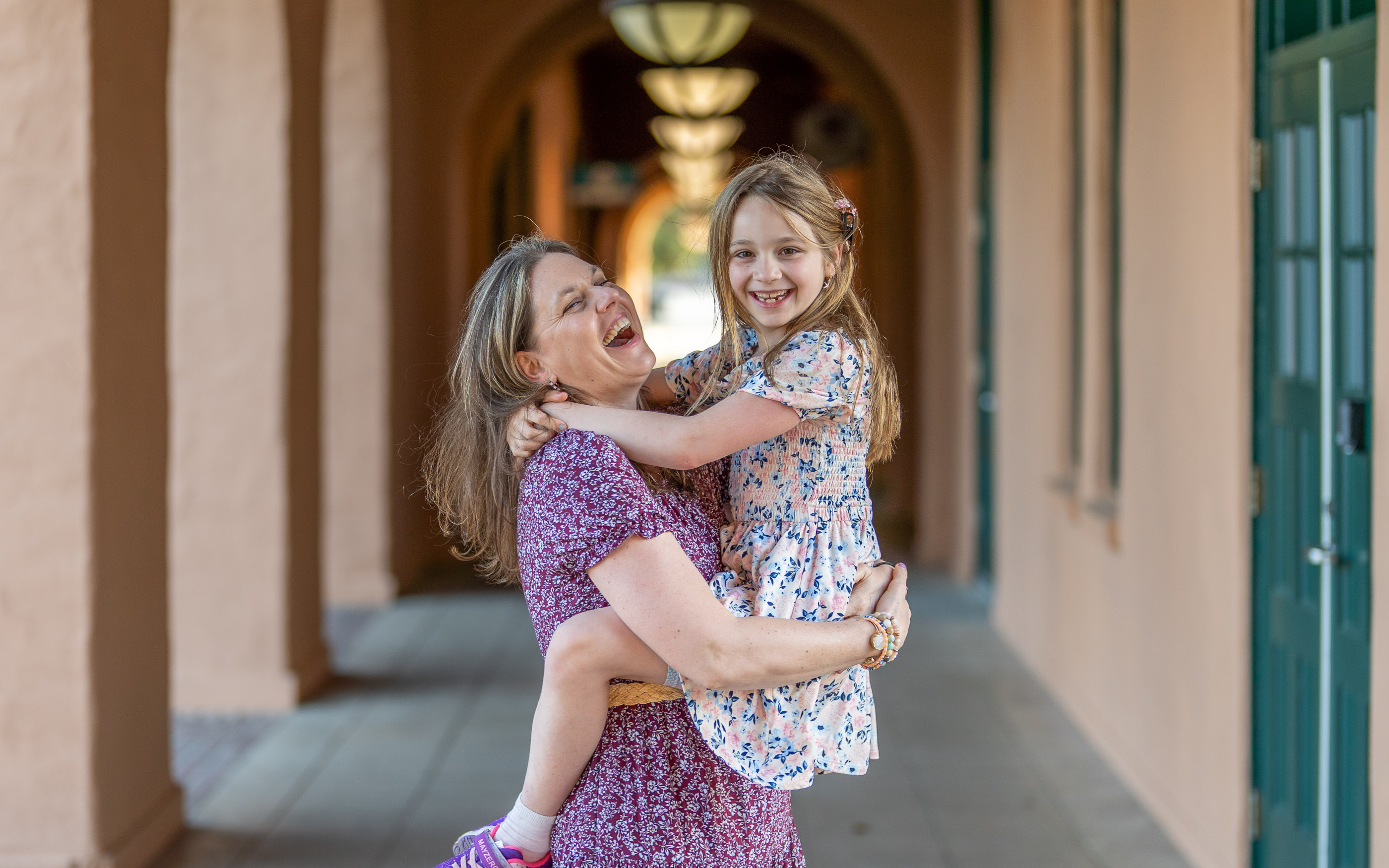 Two sisters smiling and hugging each other in an outdoor archway