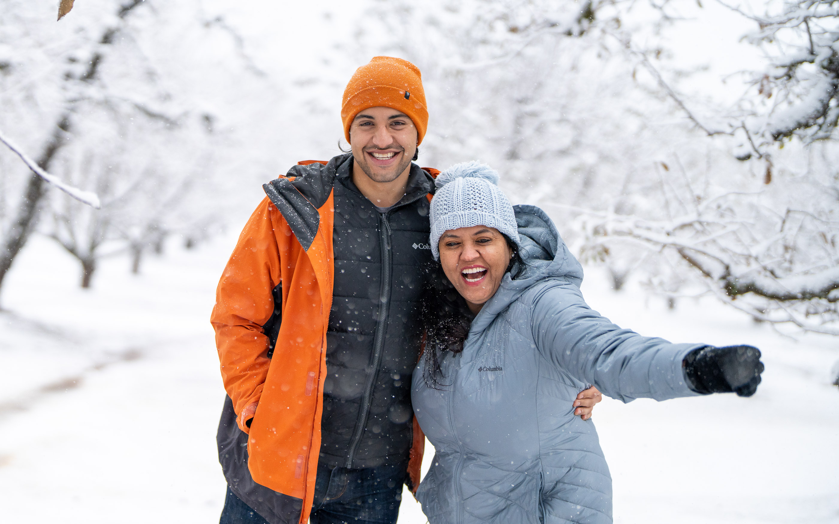 Couple smiling together in a snowy forest wearing warm winter clothing