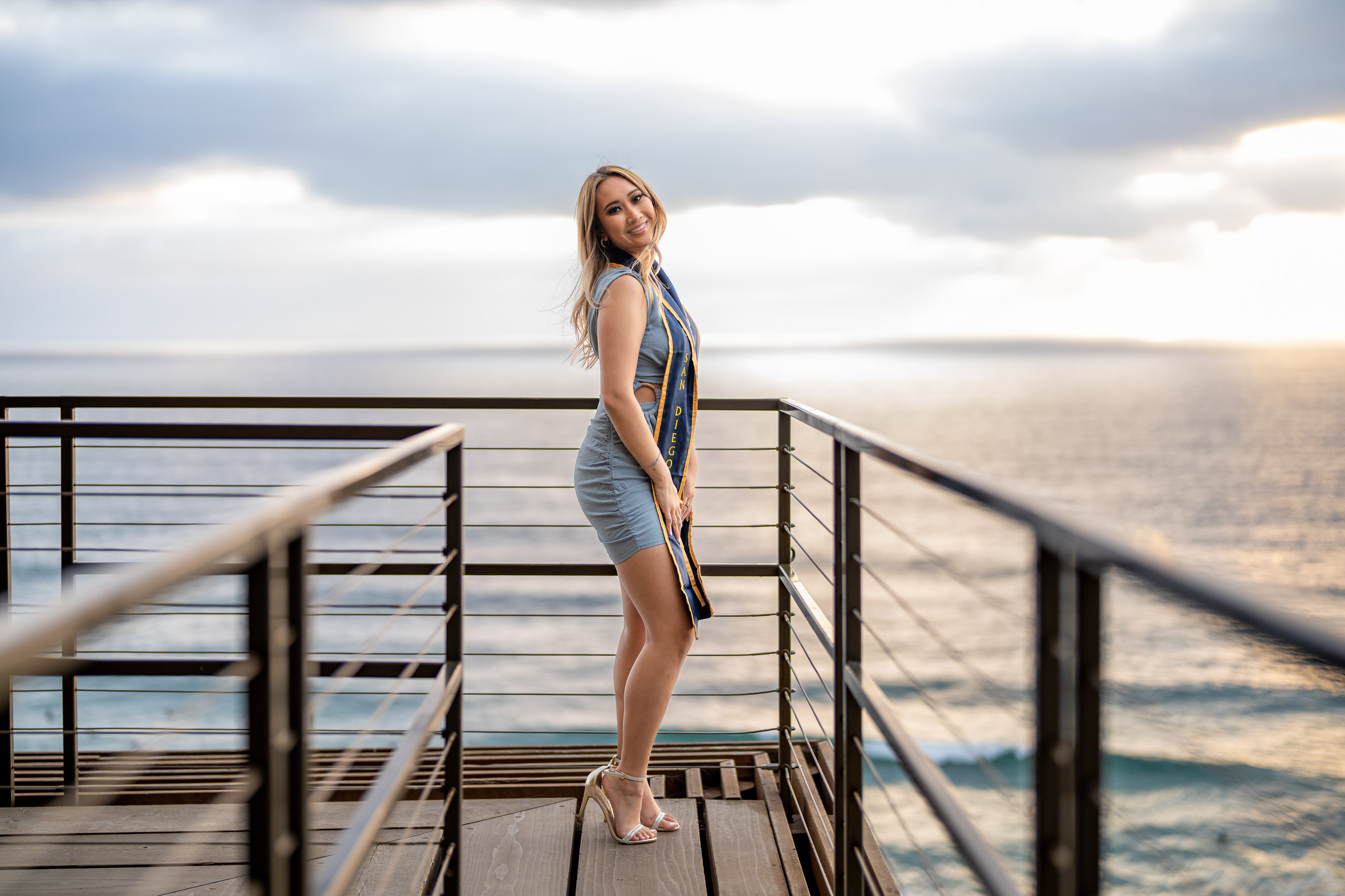 Graduate posing on a wooden pier overlooking the ocean