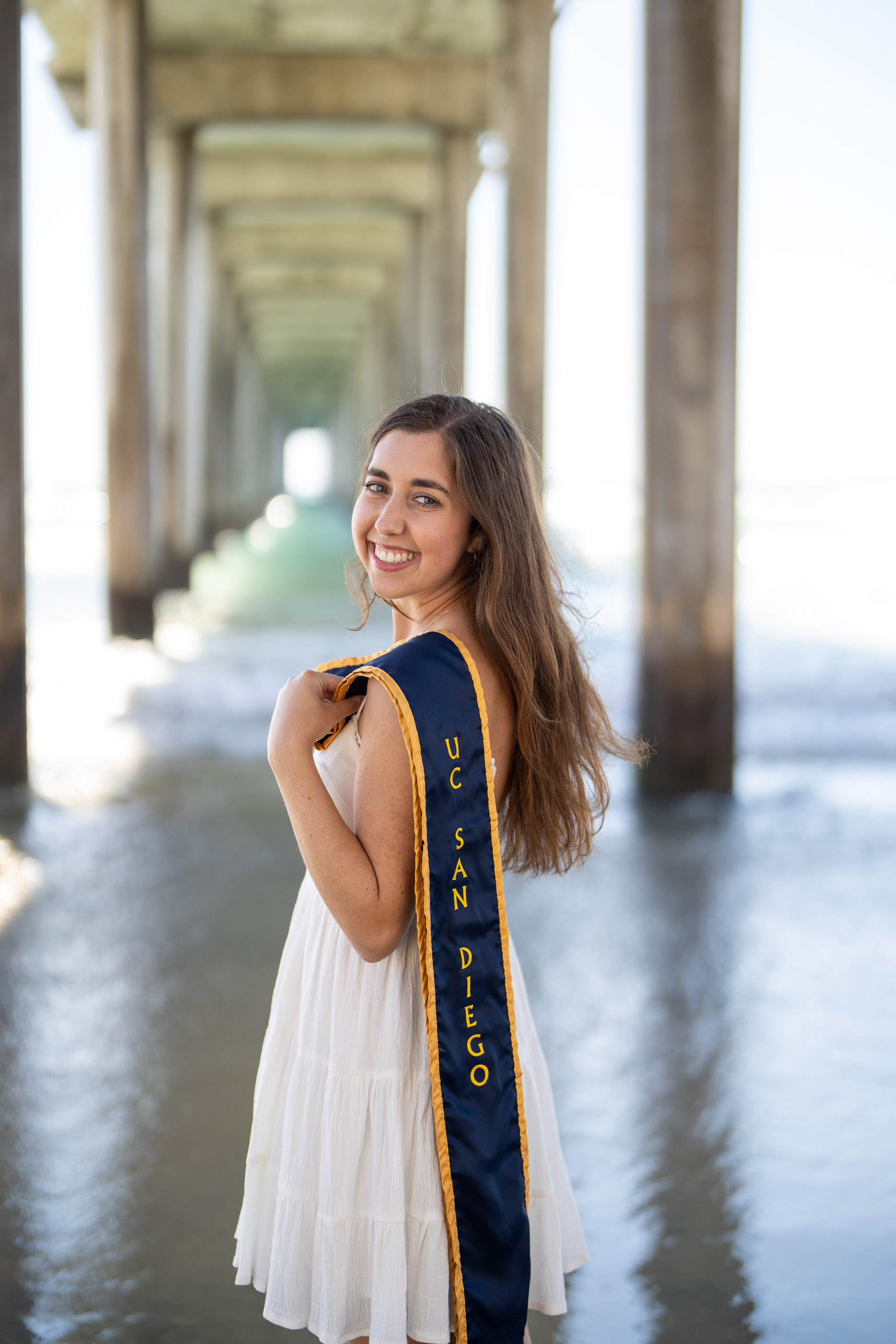 Graduate smiling in cap and gown beneath a covered outdoor walkway