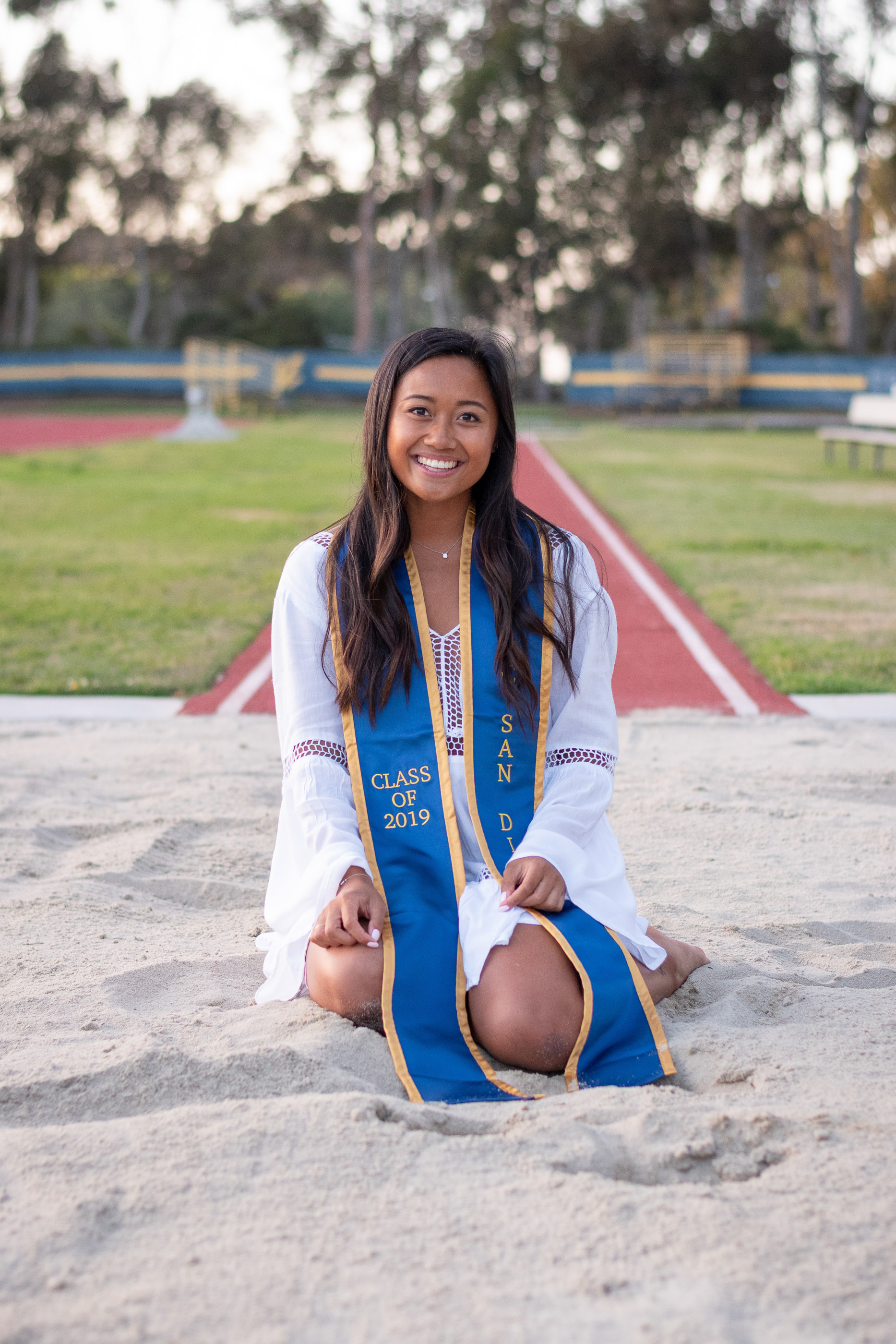 Graduate sitting on the beach in cap and gown near the ocean