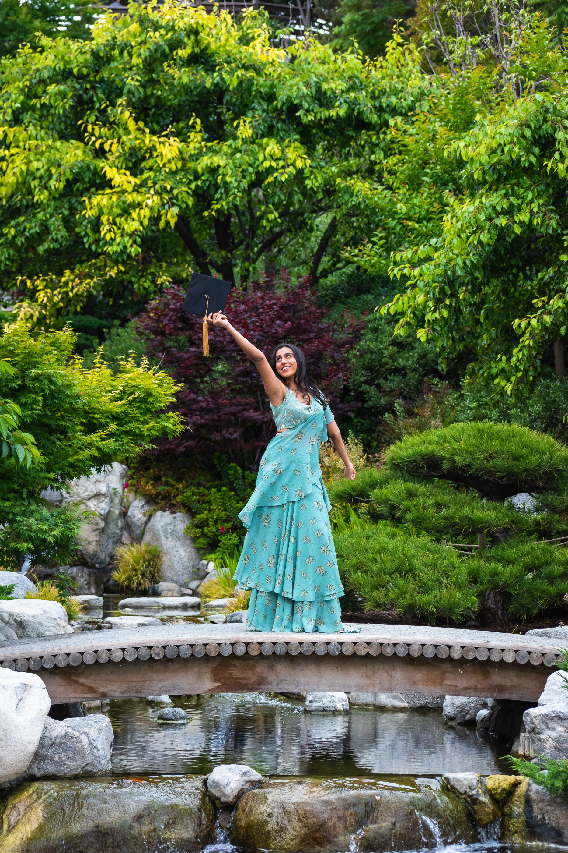 Graduate posing with a diploma beneath lush greenery in a botanical garden