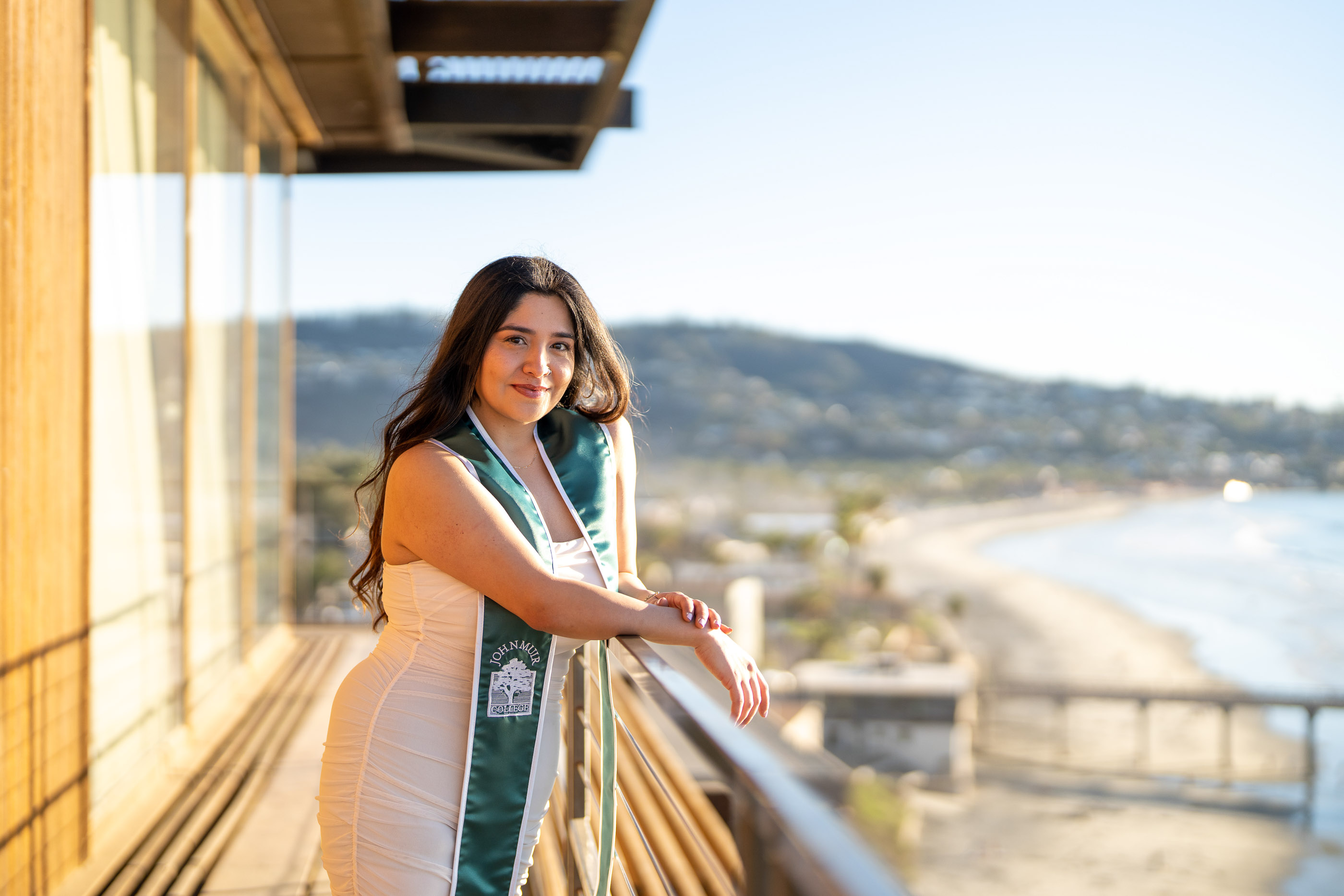 Graduate in cap and gown standing beside a coastal walkway