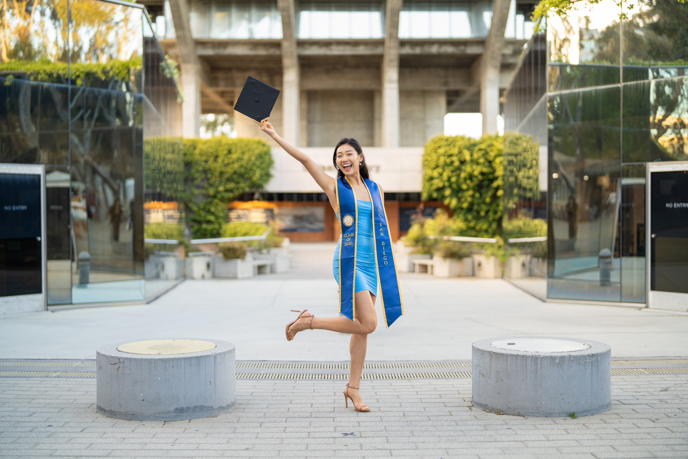 Graduate celebrating in cap and gown in a modern outdoor campus courtyard