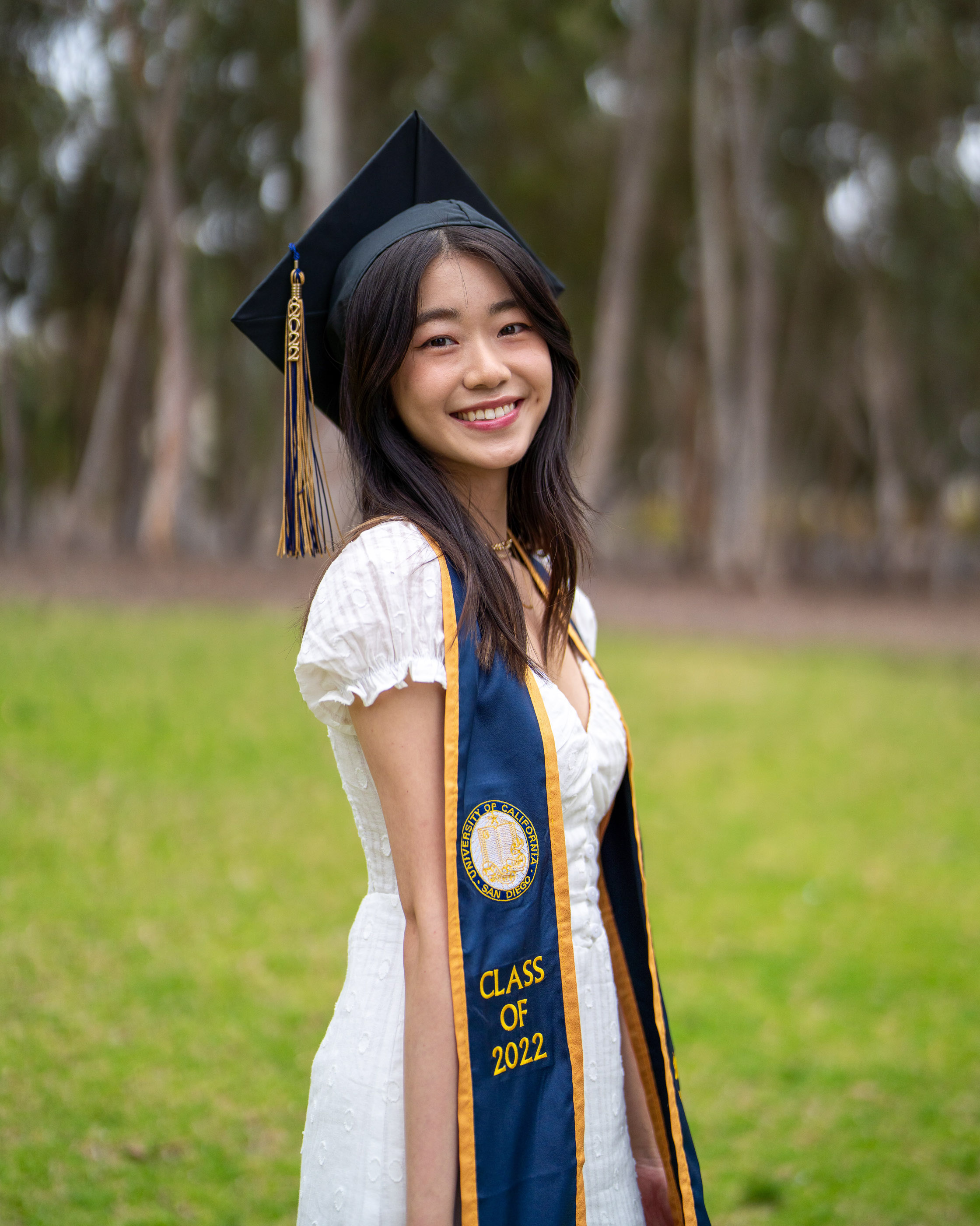 Graduate smiling in cap and gown and holding a diploma outdoors
