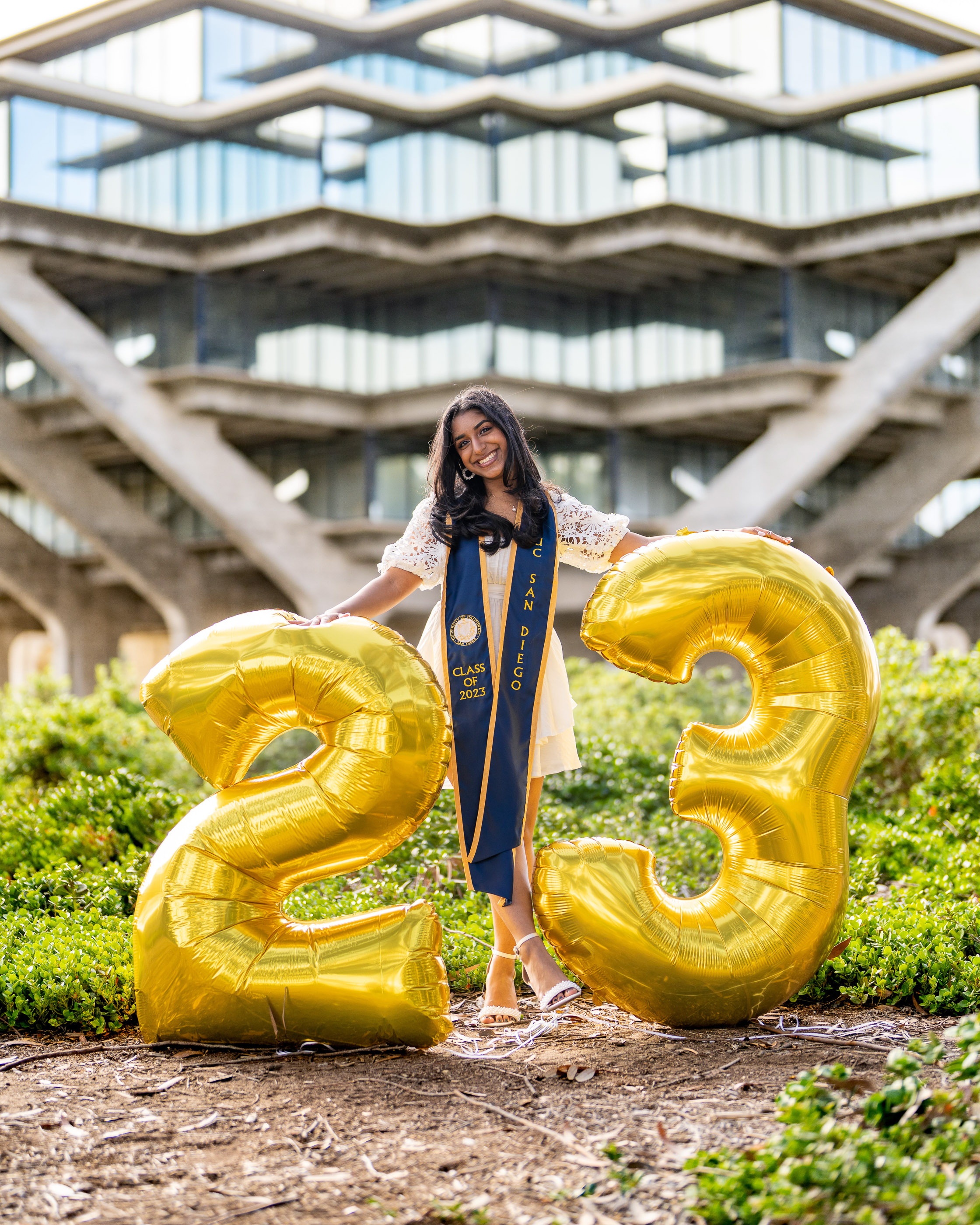 Graduate posing beside large golden graduation numbers on a university campus