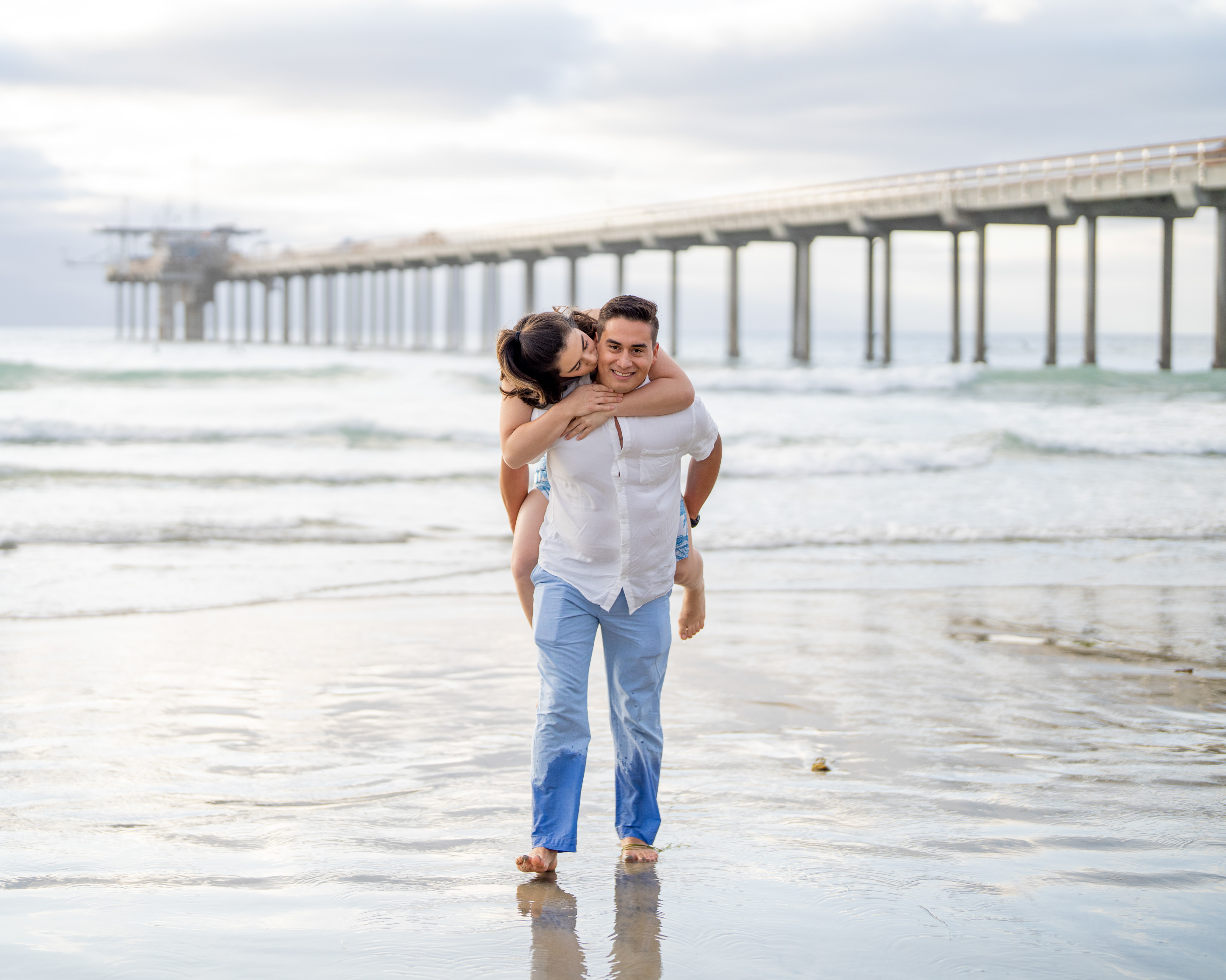 Couple walking through the shallow ocean at La Jolla Shores with Scripps Pier in the background.