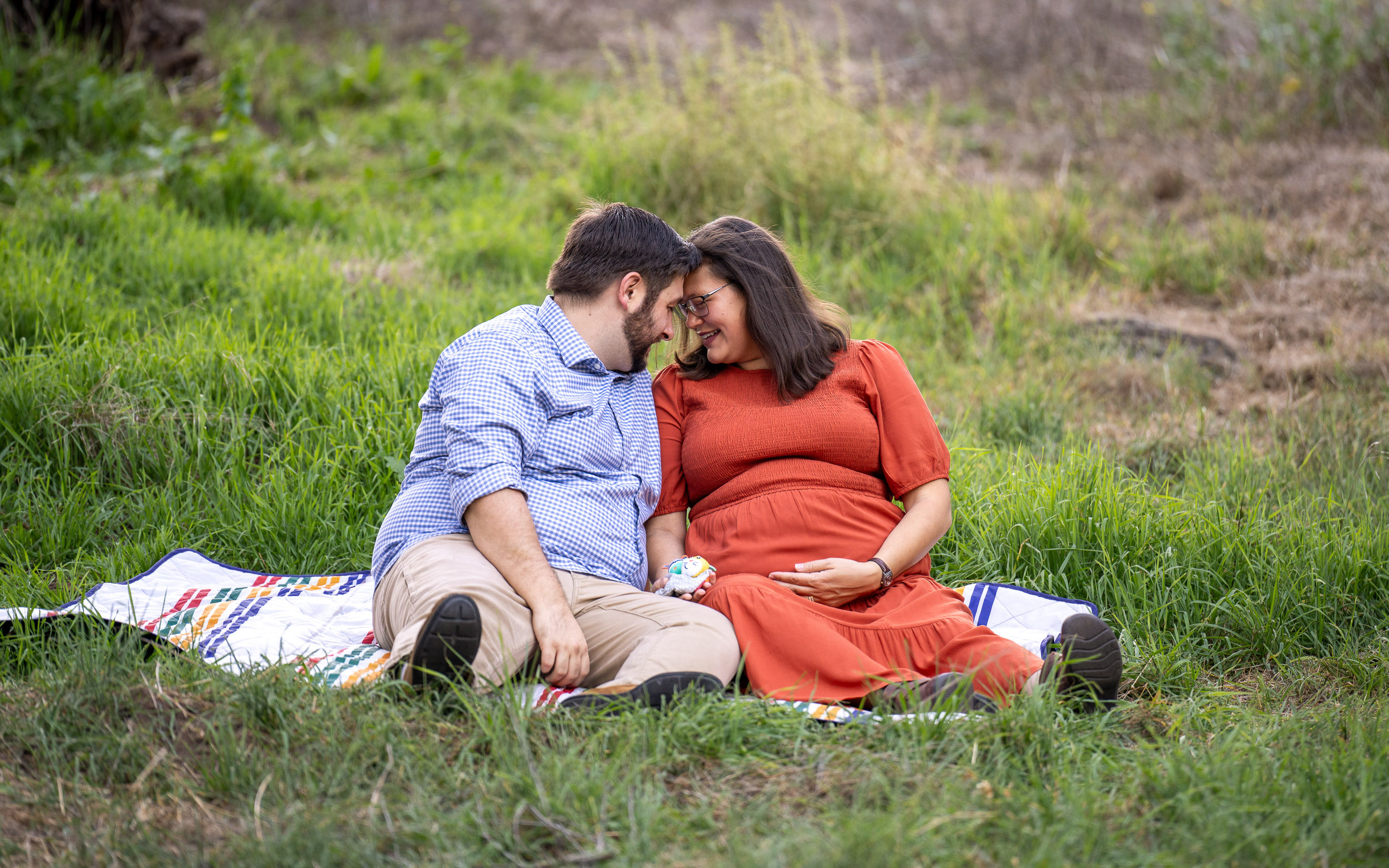 Expecting couple sitting together on a grassy hillside and embracing
